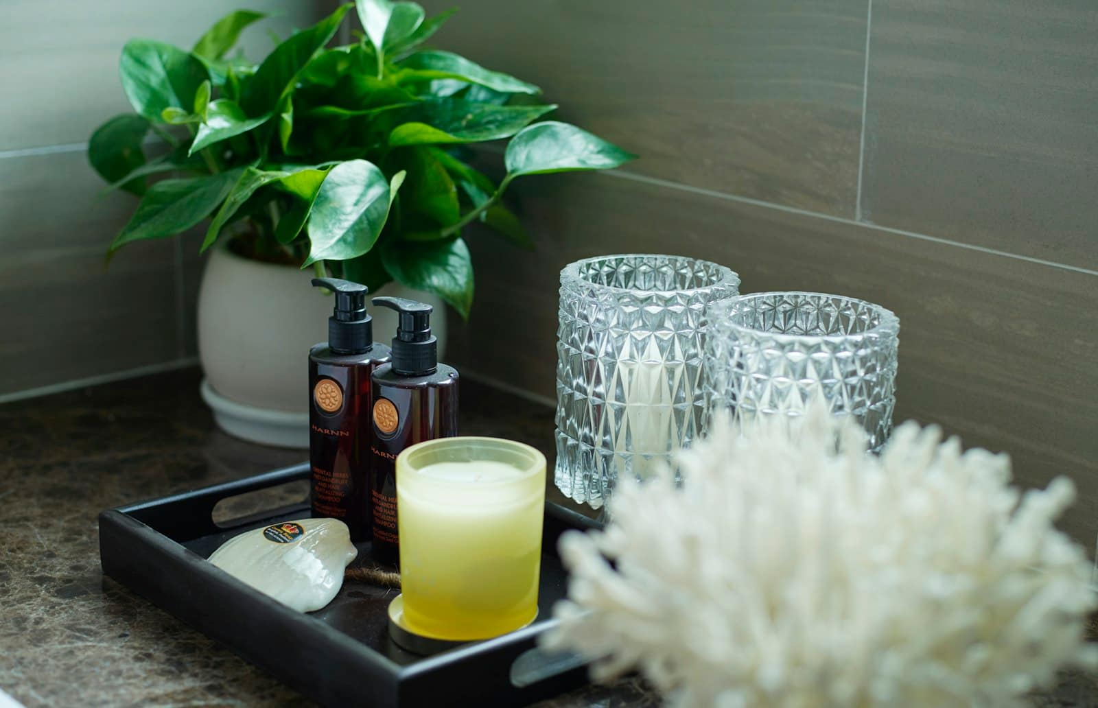 A bathroom counter tray with amber bottles, a candle, glass votives, coral, and a plant