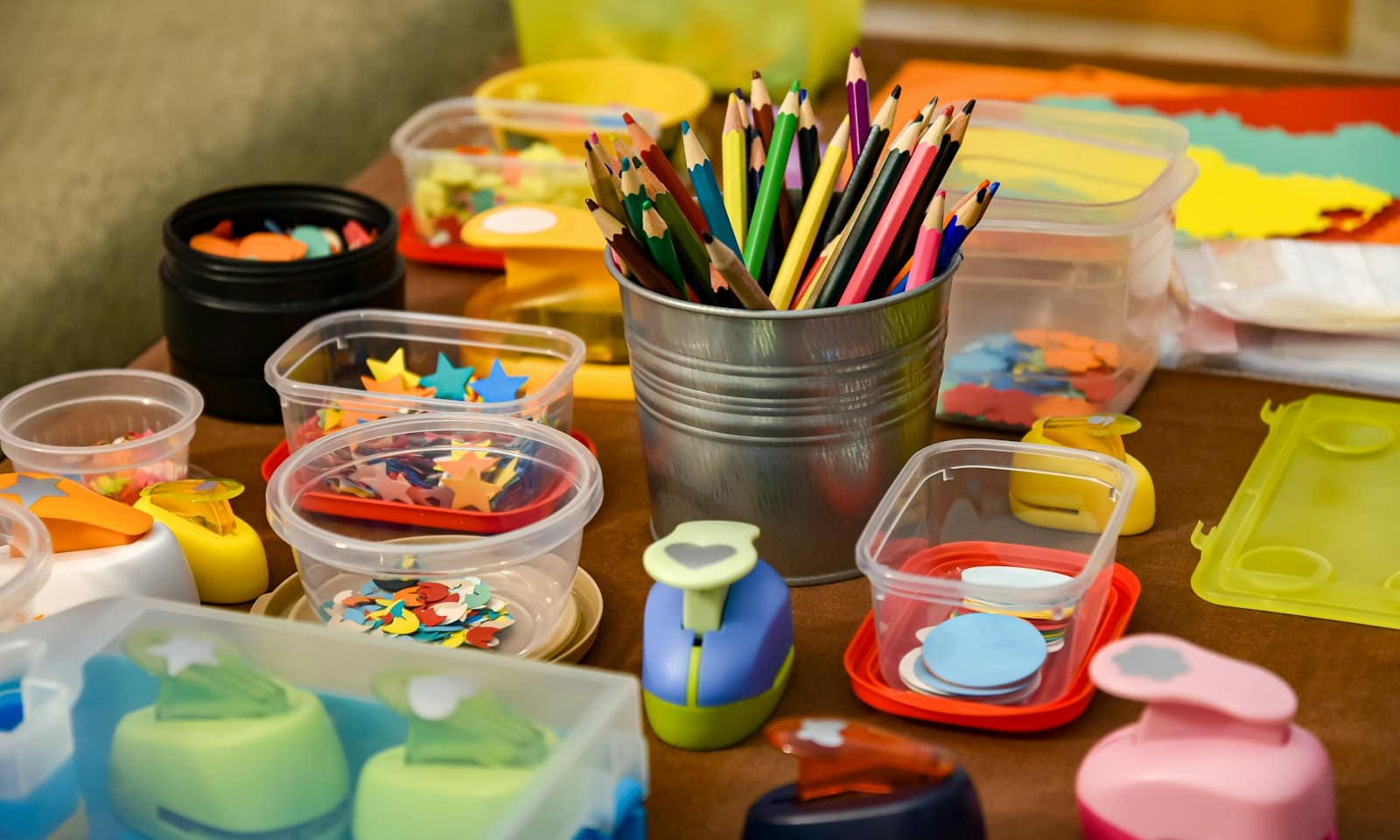 Colored pencils, paper punches, and small containers of craft pieces on a work table