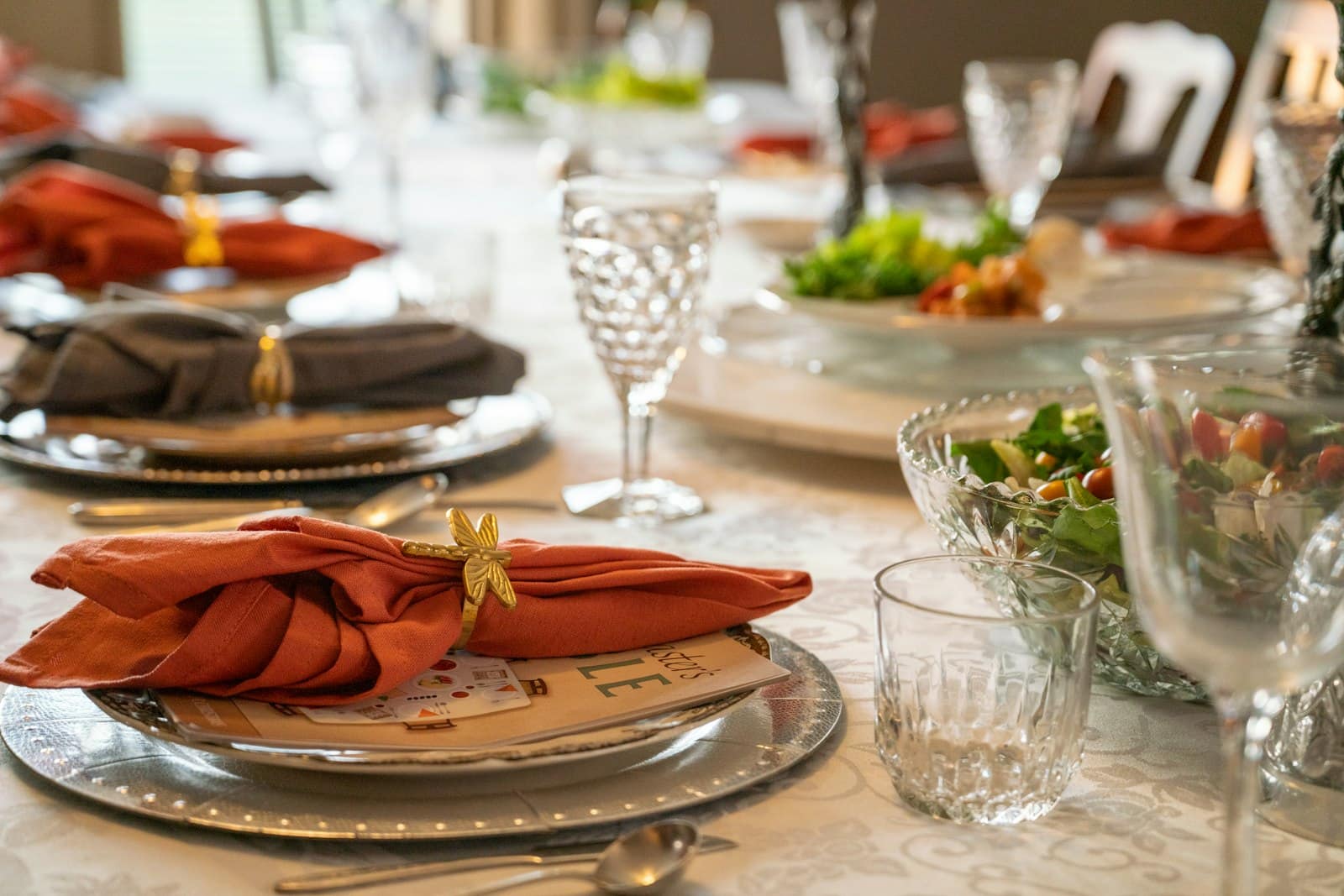 A dinner table set for guests with rust napkins, cut glassware, and shared salads