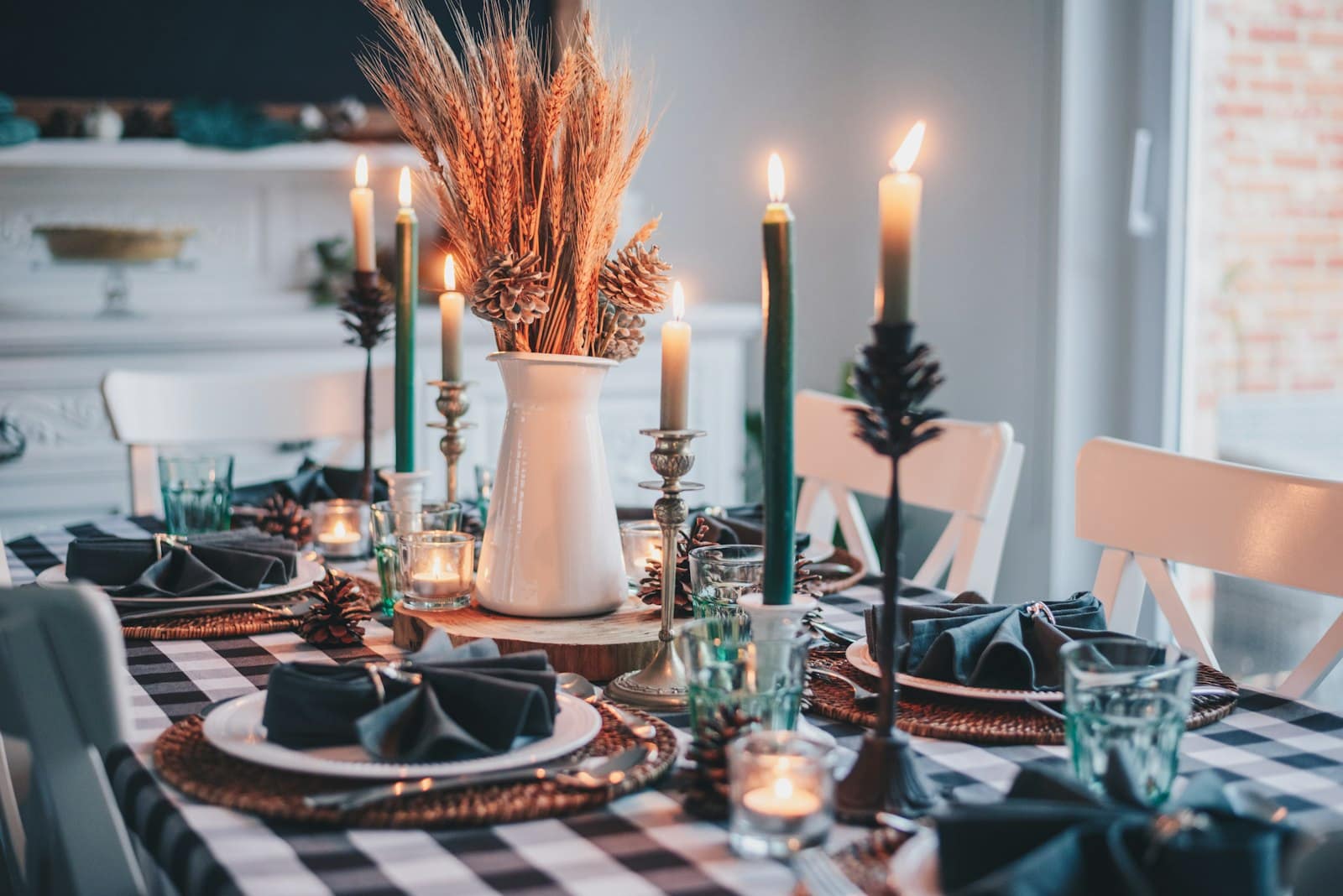 A fall table set with a buffalo-check cloth, dried wheat, taper candles, and folded napkins