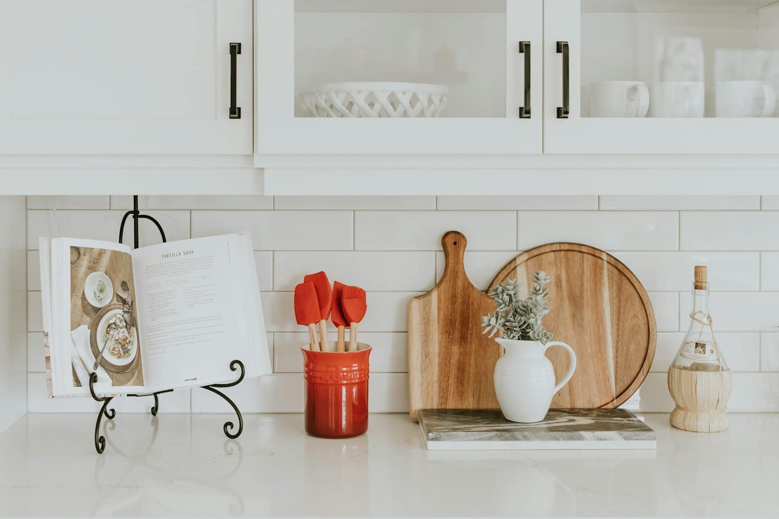 A clean white kitchen counter with a cookbook stand, cutting boards, and a utensil crock